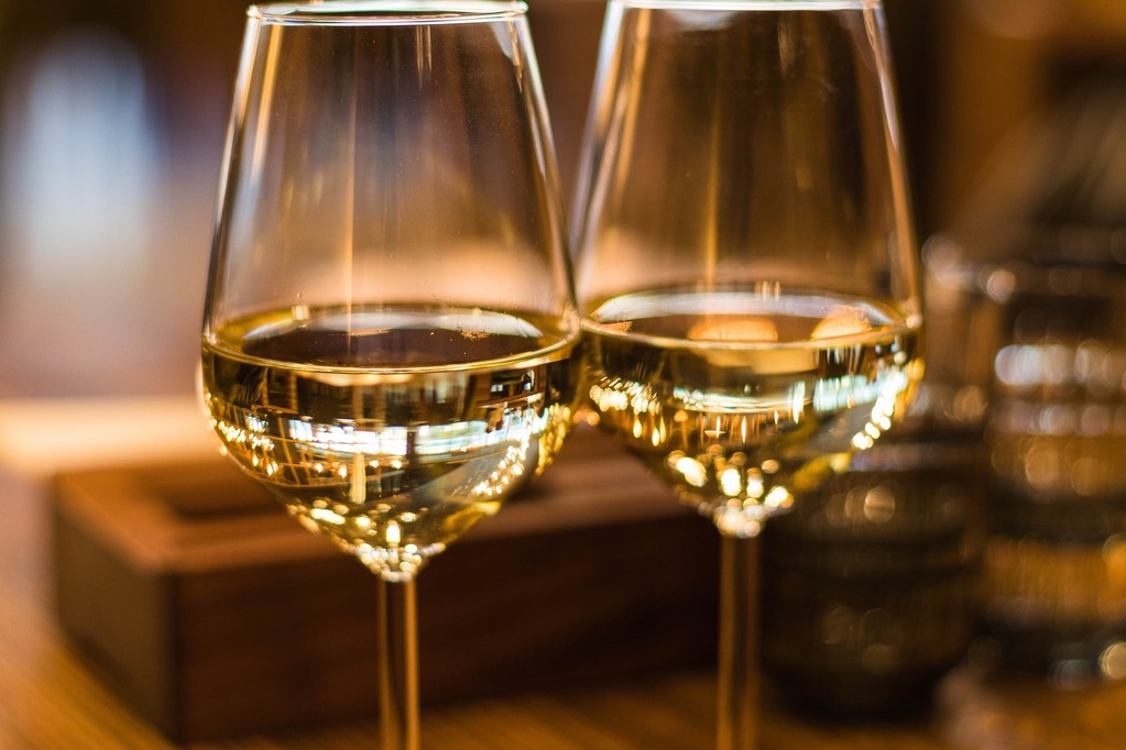 Zwei Weingläser mit Weißwein im Vordergrund und Holzelementen im Hintergrund.