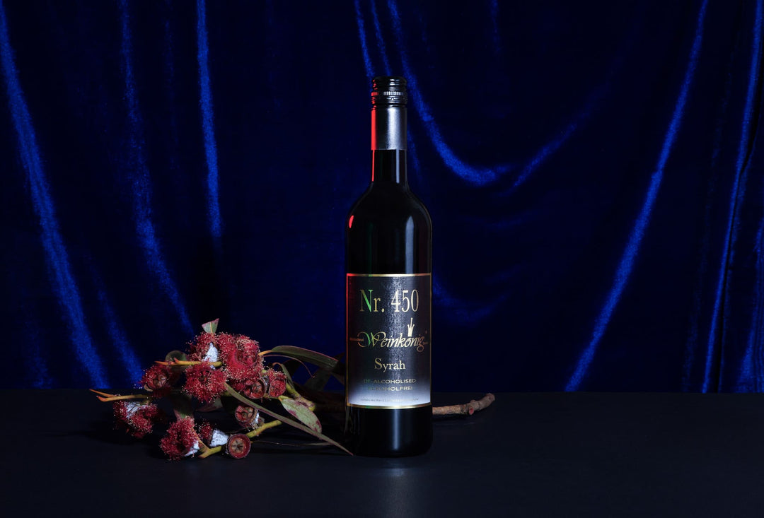 Eine Flasche Weinkönig Syrah mit dunkelblauen und roten Gestaltungselementen